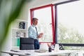 Senior business man holding a coffee cup and taking a phone call on his smart phone whilst standing in his office Royalty Free Stock Photo