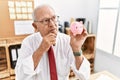 Senior business man holding piggy bank serious face thinking about question with hand on chin, thoughtful about confusing idea Royalty Free Stock Photo