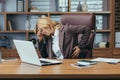 Senior business woman in a suit sitting at a desk in the office holding her hand on her back and head and suffering from Royalty Free Stock Photo