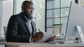 Senior businessman african american right-handed employee designer sit in office look at computer screen writing new