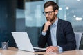 Senior businessman in glasses and beard is thinking about a decision, man is working inside the office and using laptop Royalty Free Stock Photo