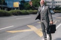 Senior businessman with laptop bag gesturing while hailing for taxi cab in the city streets Royalty Free Stock Photo