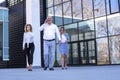 Senior businessman and two young businesswomen walking outside the building on a break