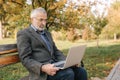 Senior businessman using laptop outside. Elderly man in gray jacket use laptop in the park Royalty Free Stock Photo