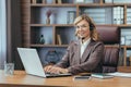 Senior businesswoman with headset working at laptop in home office setting Royalty Free Stock Photo