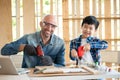 A senior carpenter and boy wearing goggle in the modern wood workplace and holding screwdriver. A man and boy looking forward and