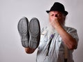 Senior Caucasian bearded male covering his nose while holding stinky shoes