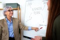 Senior caucasian business woman showing young female coworker business plan on white board in the office Royalty Free Stock Photo