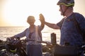 Senior caucasian couple riding off road on the pebble beach with bicycles at sunset giving high five smiling. Authentic elderly Royalty Free Stock Photo