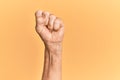 Senior caucasian hand over yellow isolated background doing protest and revolution gesture, fist expressing force and power