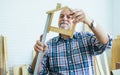 Senior Caucasian happy retired old male woodworker or carpenter smiling with happiness, wearing check shirt, measure to create DIY