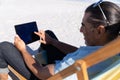 Senior Caucasian man sitting on a deck chair and using a digital tablet at the beach Royalty Free Stock Photo