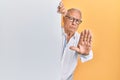 Senior caucasian man holding blank empty banner with open hand doing stop sign with serious and confident expression, defense Royalty Free Stock Photo