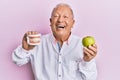 Senior caucasian man holding denture and green apple smiling and laughing hard out loud because funny crazy joke