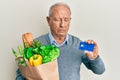 Senior caucasian man holding groceries and credit card depressed and worry for distress, crying angry and afraid Royalty Free Stock Photo