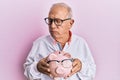 Senior caucasian man holding piggy bank with glasses depressed and worry for distress, crying angry and afraid Royalty Free Stock Photo