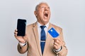 Senior caucasian man holding smartphone and credit card angry and mad screaming frustrated and furious, shouting with anger Royalty Free Stock Photo