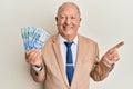 Senior caucasian man holding south african 20 rand banknotes smiling happy pointing with hand and finger to the side