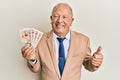 Senior caucasian man holding united kingdom pounds smiling happy and positive, thumb up doing excellent and approval sign