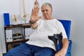 Senior caucasian man at physiotherapy clinic holding crutches doing stop sing with palm of the hand Royalty Free Stock Photo