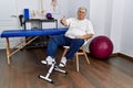 Senior caucasian man at physiotherapy clinic using pedal exerciser smiling friendly offering handshake as greeting and welcoming Royalty Free Stock Photo