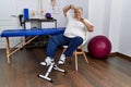 Senior caucasian man at physiotherapy clinic using pedal exerciser smiling making frame with hands and fingers with happy face