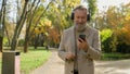 Senior Caucasian man 60s old male walk in autumn park city listening music in wireless headphones dancing watching Royalty Free Stock Photo