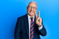 Senior caucasian man wearing business suit and tie smiling looking to the camera showing fingers doing victory sign Royalty Free Stock Photo