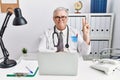 Senior caucasian man wearing doctor uniform and stethoscope at the clinic smiling with happy face winking at the camera doing Royalty Free Stock Photo