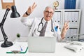 Senior caucasian man wearing doctor uniform and stethoscope at the clinic smiling with tongue out showing fingers of both hands Royalty Free Stock Photo