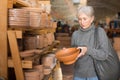 Aged woman choosing earthenware crockery in store
