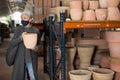 Aged woman in mask choosing earthenware crockery in store