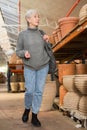 Aged woman choosing earthenware crockery in store