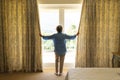 Senior caucasian woman standing next to window and widening courtains in bedroom