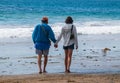 Senior citizen baby boomer male and female caucasian couple walking on the beach towards the ocean holding hands. Royalty Free Stock Photo