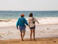 Senior citizen baby boomer male and female caucasian couple walking on the beach towards the ocean holding hands and pointing. Royalty Free Stock Photo