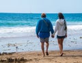 Senior citizen baby boomer male and female caucasian couple walking on the beach towards the ocean holding hands. Royalty Free Stock Photo