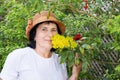 Senior citizen brunette woman in wicker hat stands and sniffs yellow flowers from the bush in her garden Royalty Free Stock Photo