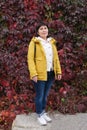 Senior citizen woman against a wall of red autumn vine leaves