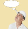 Senior construction worker with hardhat looking up over yellow background