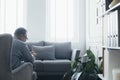 Counselor sitting in grey wing back chair in elegant Scandinavian interior waiting for a patient