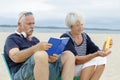 senior couple on beach reading book and applying suncream Royalty Free Stock Photo