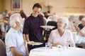 Senior Couple Being Served With Meal By Carer In Dining Room Of Retirement Home