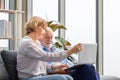 Senior couple checking their bills, man and a woman Using laptop on a cozy sofa at home, retired elderly family reading documents Royalty Free Stock Photo