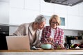 Senior couple cooking dinner together in the kitchen for golden wedding anniversary, reading recipe from internet on laptop. Older Royalty Free Stock Photo