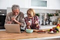 Senior couple cooking dinner together in the kitchen for golden wedding anniversary, reading recipe from internet on laptop. Older Royalty Free Stock Photo