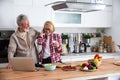 Senior couple cooking dinner together in the kitchen for golden wedding anniversary, reading recipe from internet on laptop. Older Royalty Free Stock Photo