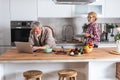 Senior couple cooking dinner together in the kitchen for golden wedding anniversary, reading recipe from internet on laptop. Older Royalty Free Stock Photo