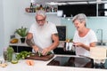 Senior couple cooking at home while preparing vegetarian lunch - Mature people cutting vegetables for healthy meal inside house