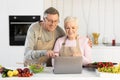 Senior Couple Cooking And Using Laptop Preparing Dinner In Kitchen Royalty Free Stock Photo